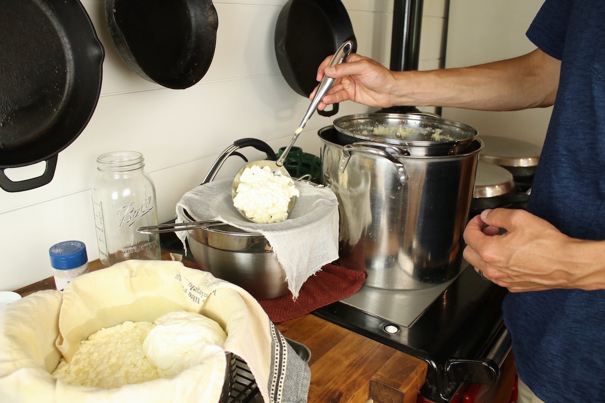 scooping curd into strainer to strain whey