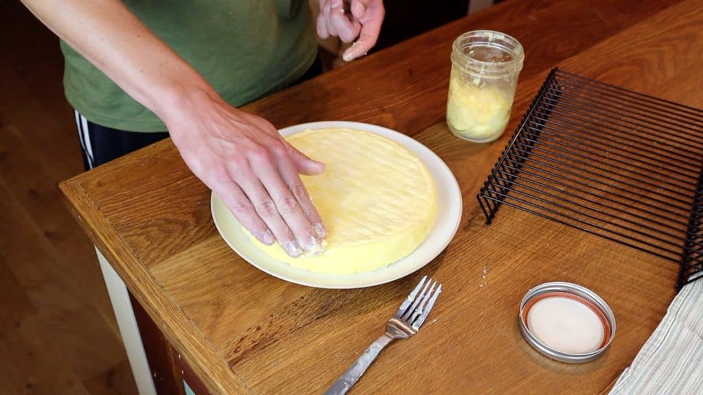 spreading butter on wheel of cheese