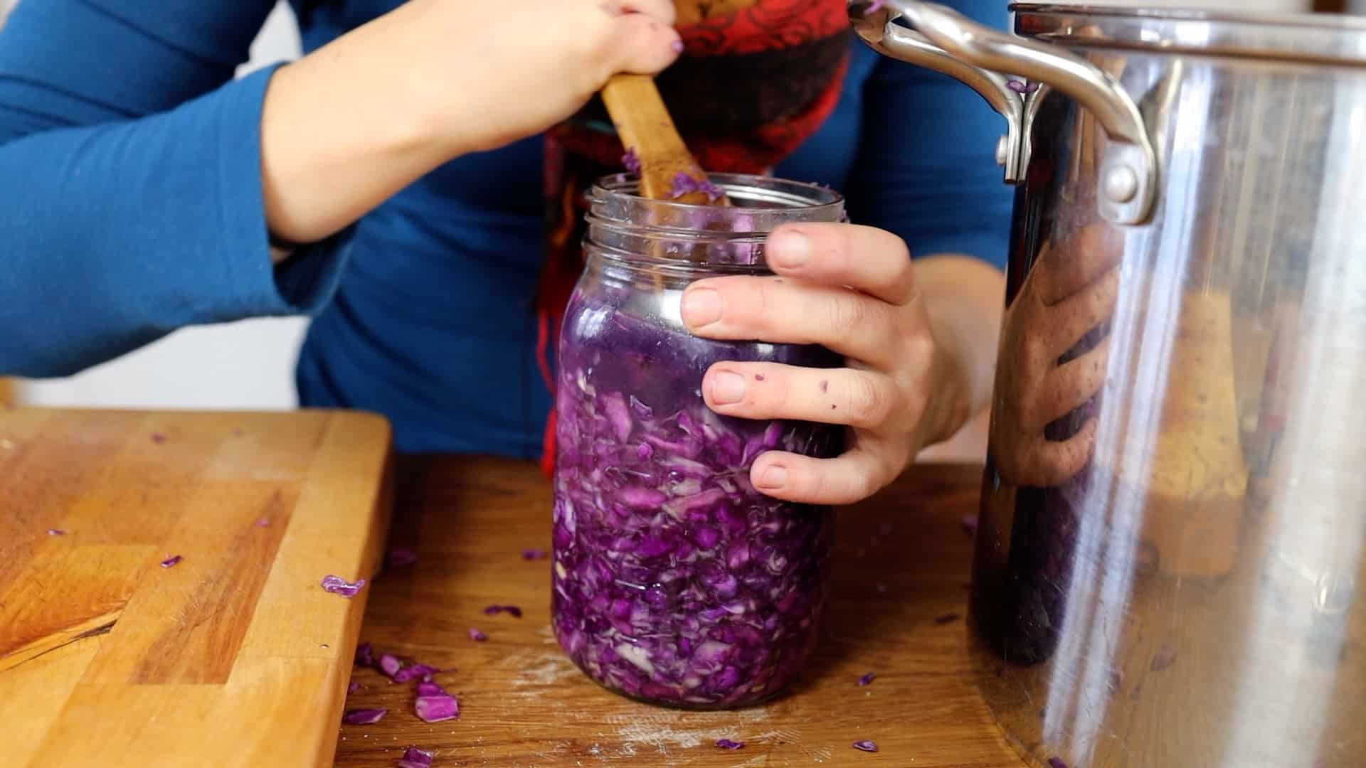 pressing red cabbage in jar to release liquid