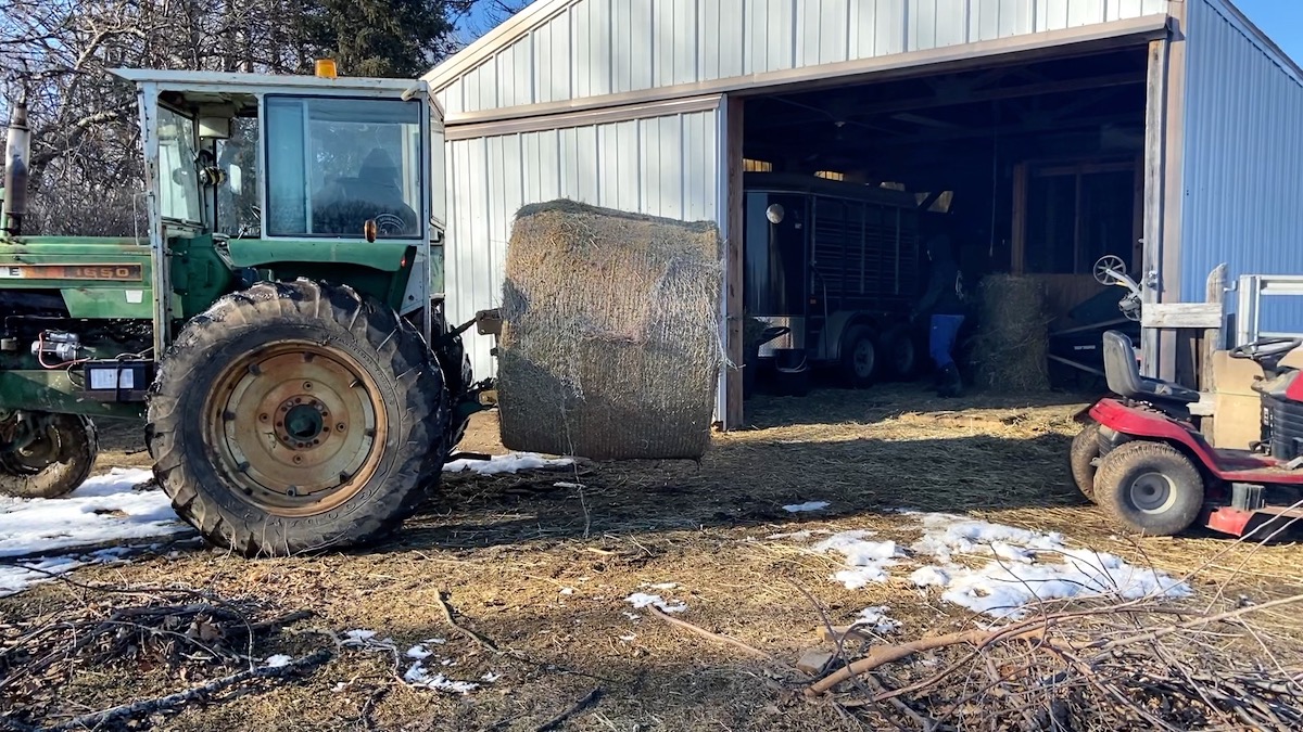 tractor dropping round hay bale in barn