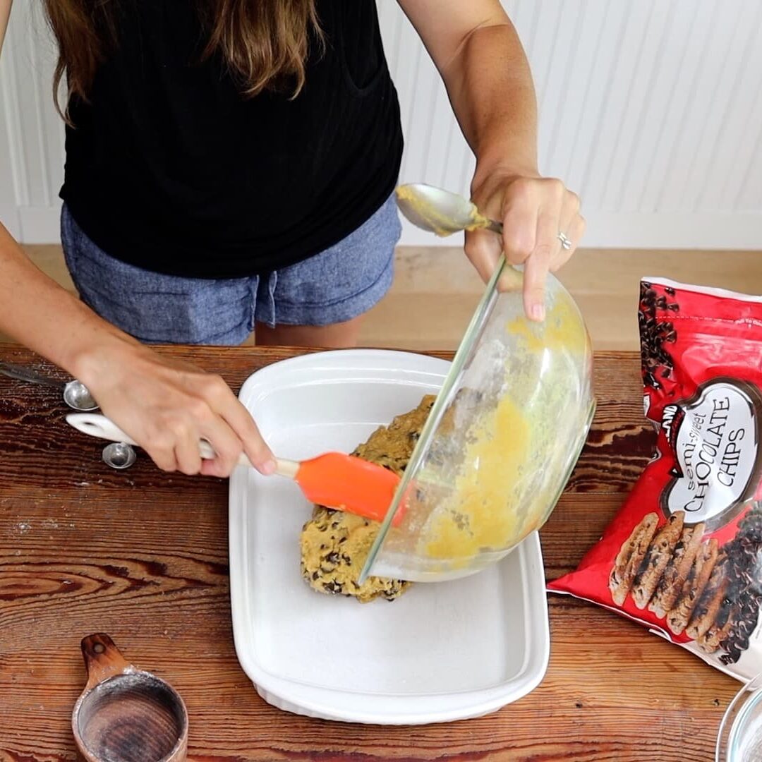 adding cookie cake batter to greased pan