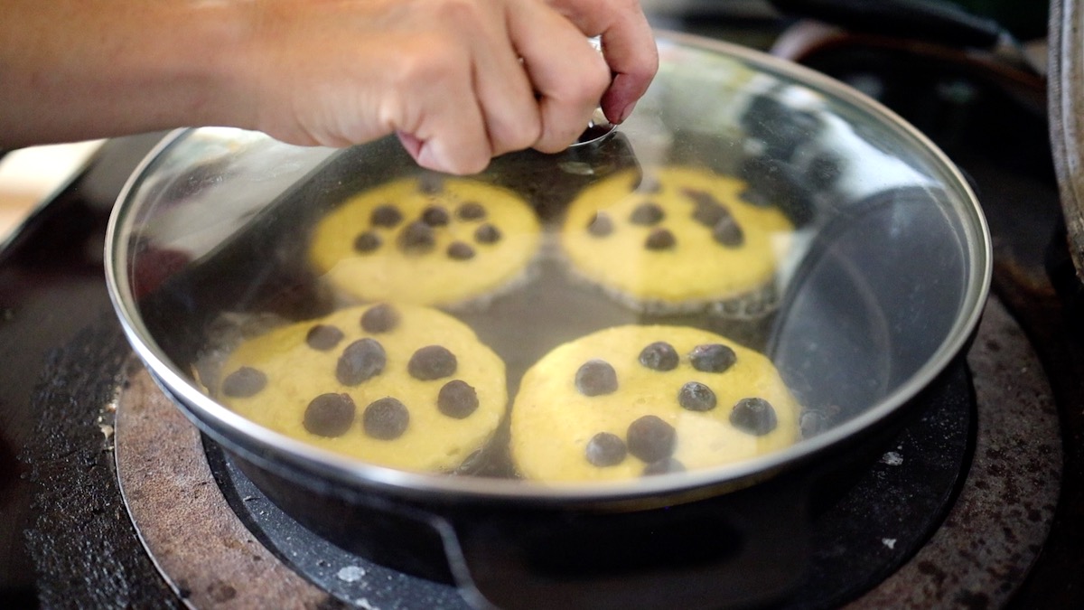 placing cover on top of pancakes in pan