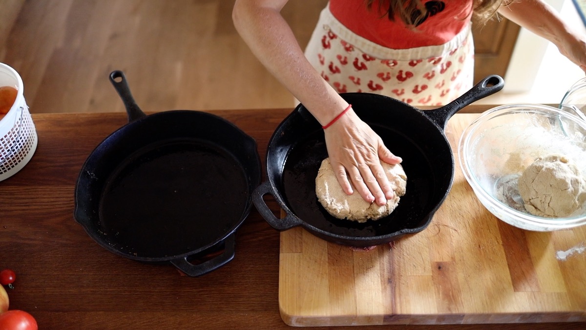 spreading pizza dough in cast iron pan